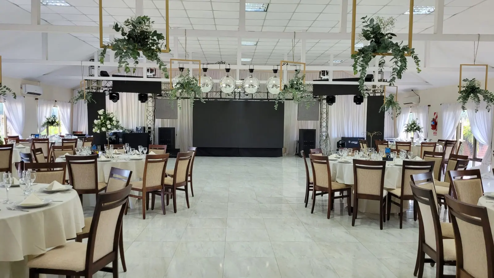 Salón armado para una fiesta con mesas redondas y escenario